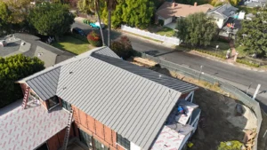 Aerial view of a light gray standing seam metal roof being finished on a two-story home