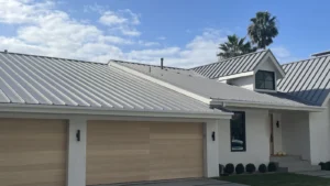 Light gray standing seam metal roof on a modern white home with a wood garage door